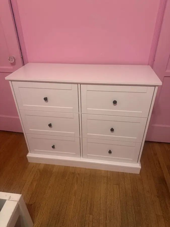 White six-drawer dresser assembled against a pink wall