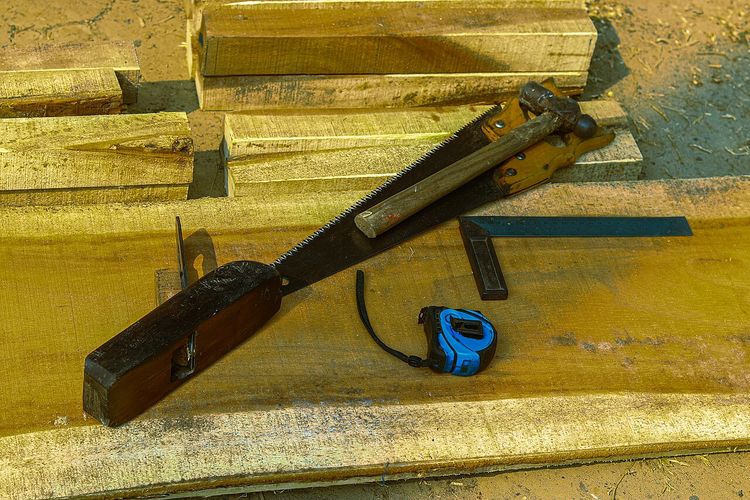 Hand saw, hammer, wood plane, steel square and tape measure laid out on wooden planks