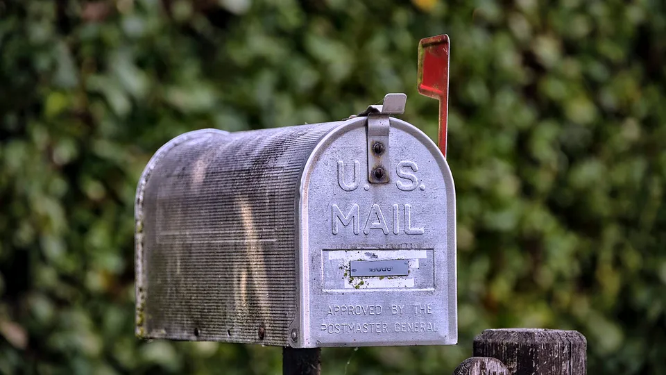Metal mailbox on a post in front of greenery