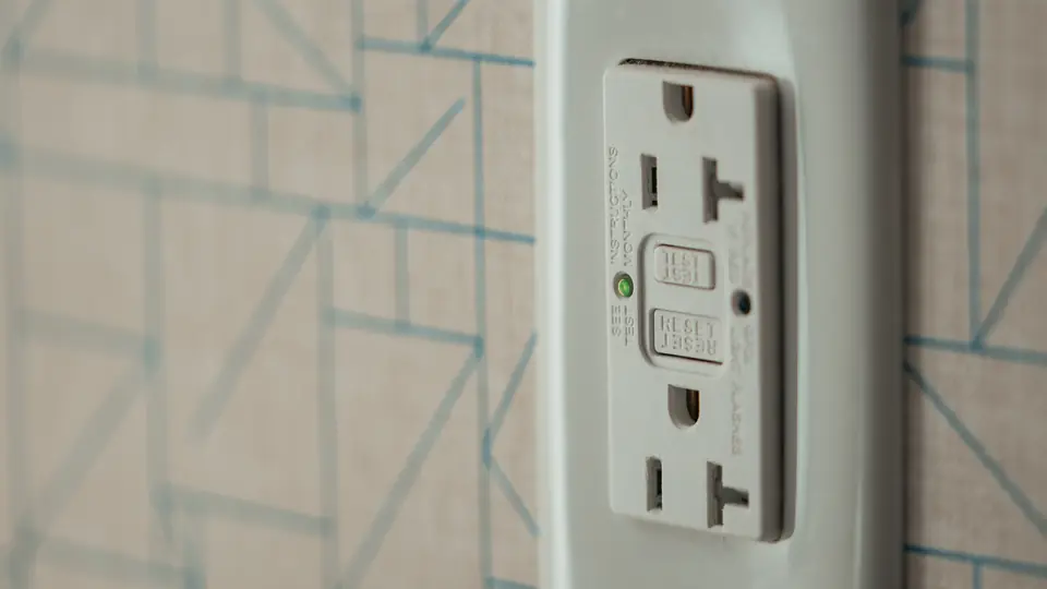 GFCI outlet with test and reset buttons on a wall with patterned wallpaper