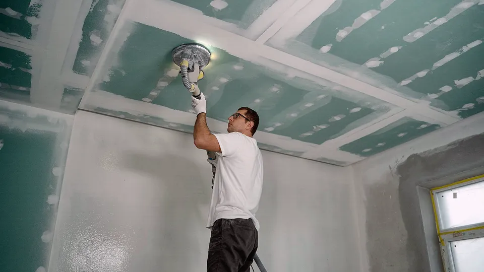 Worker sanding a ceiling in an empty room
