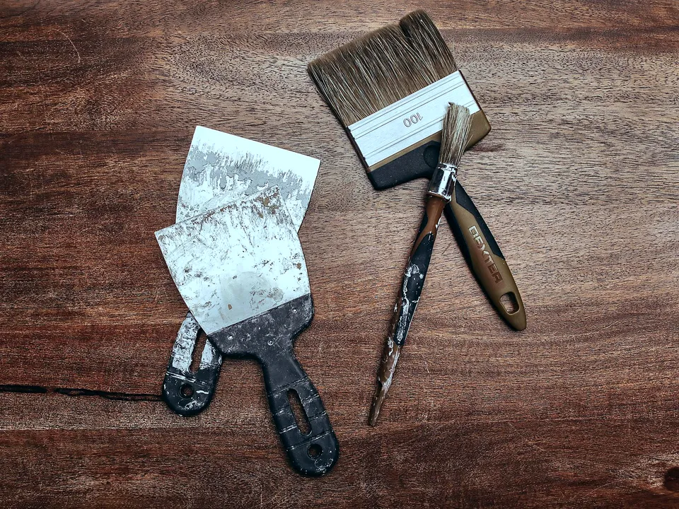 Putty knives and a paintbrush on a wood surface