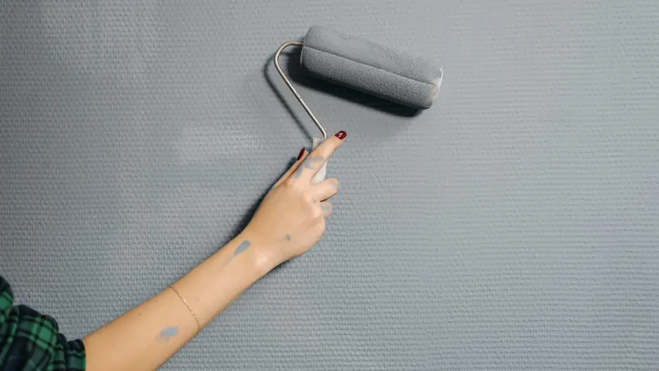 Hand rolling gray paint onto a textured interior wall