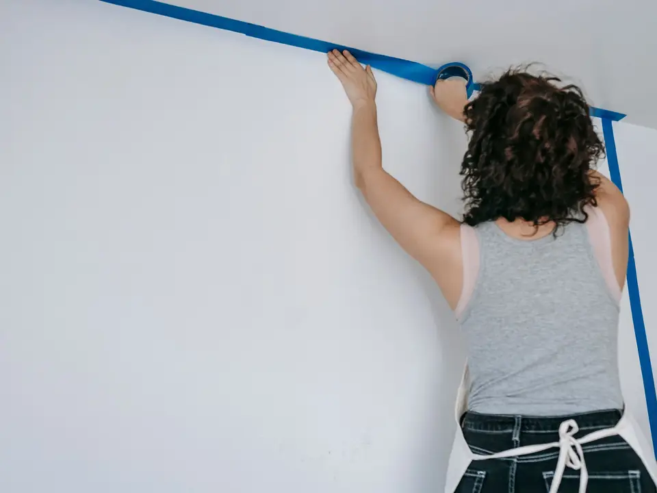 Person pressing blue painter's tape along the line where a wall meets the ceiling