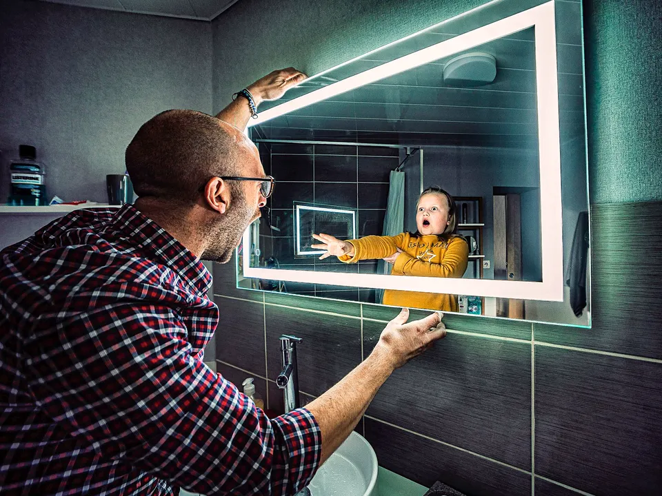 Man mounting a lighted LED mirror in a bathroom