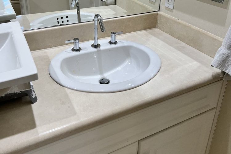 Chrome widespread faucet on a white drop-in sink set in a cream stone vanity top