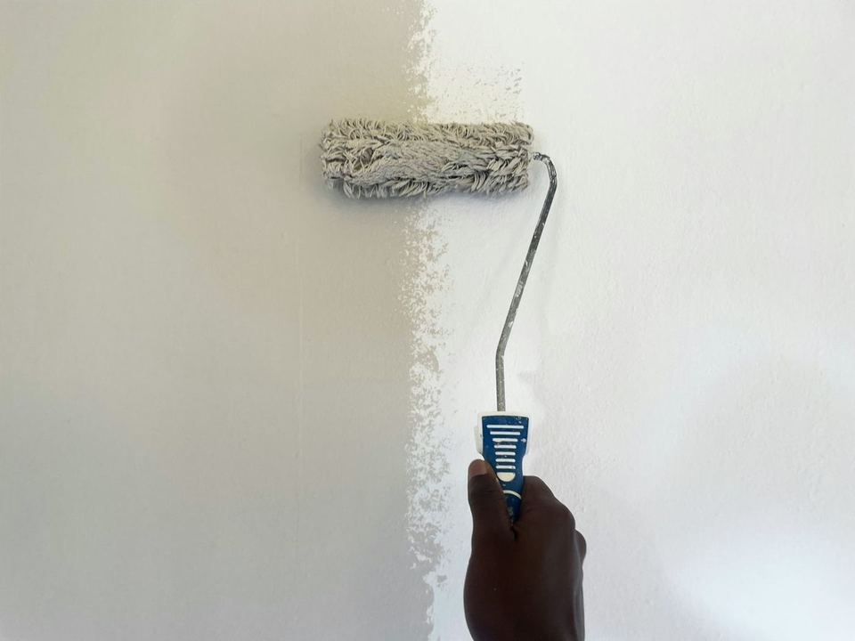 A paint roller rolling white paint on a wall