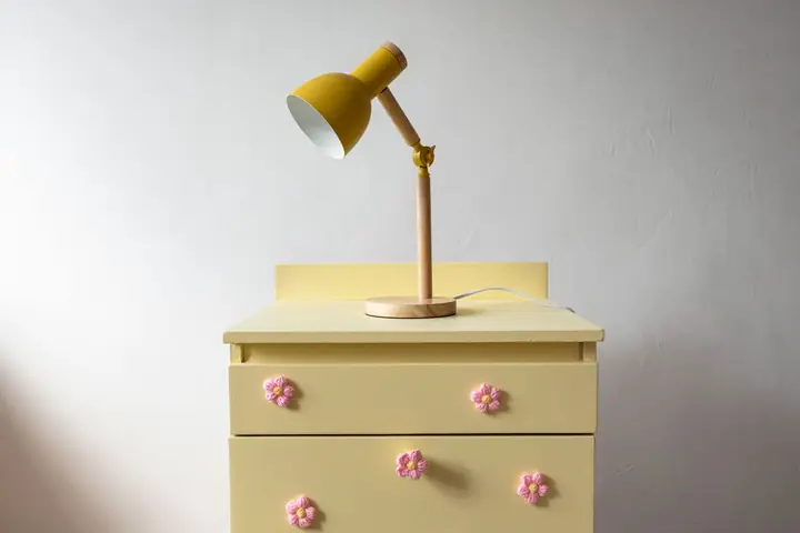 A minimalist view of a yellow lamp on a vintage dresser with floral handles in pastel tones