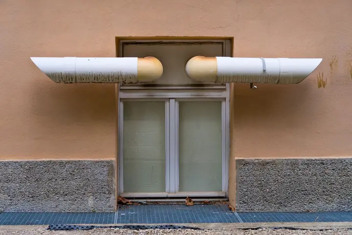 Close-up of industrial ventilation pipes above a window on a building wall