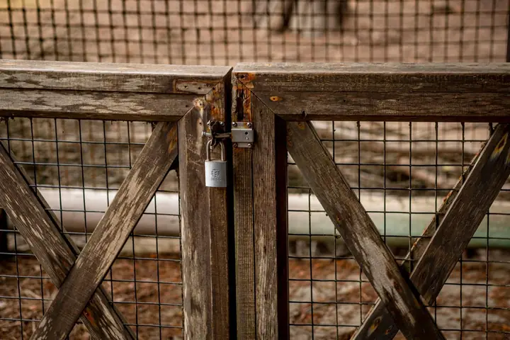 Close-up of a rustic wooden gate with a padlock, offering a secure outdoor setting