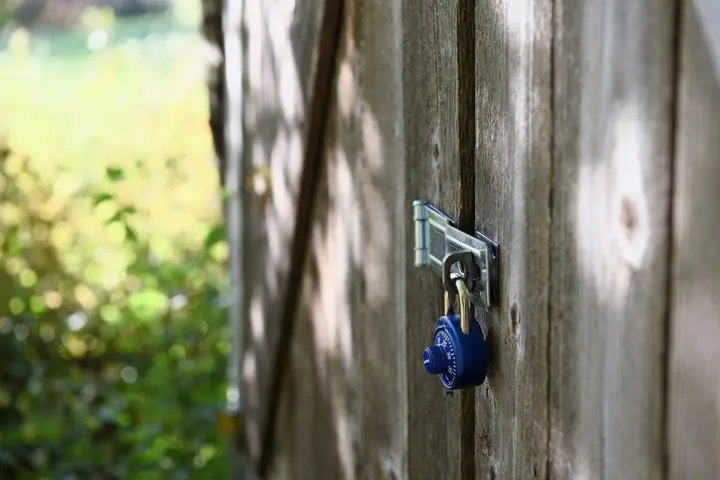 A blue padlock secures a wooden gate outdoors with sunlight filtering through