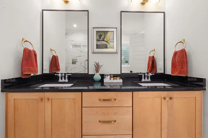 Bathroom vanity featuring dual sinks, black countertop, and mirrors