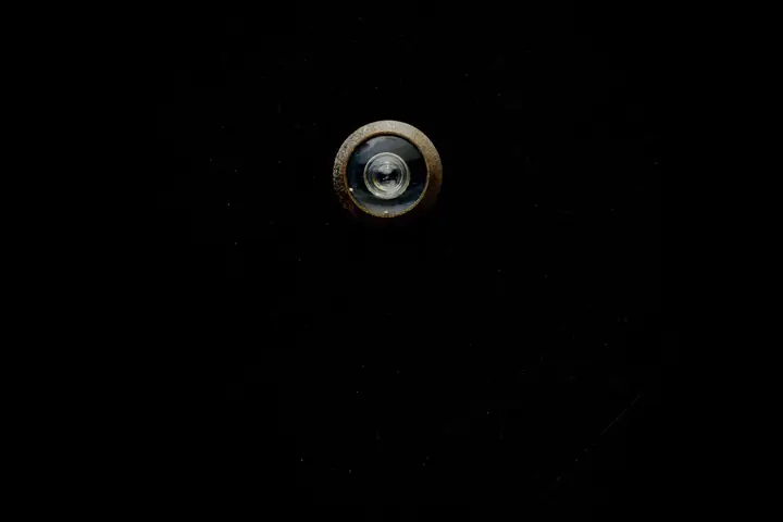 Close-up image of a metallic door peephole with a black background, offering copy space