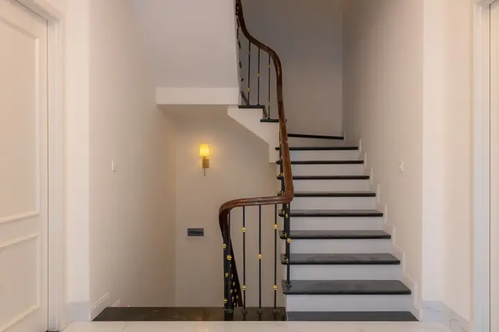 A modern staircase featuring a wooden handrail and light wall sconce in an indoor setting