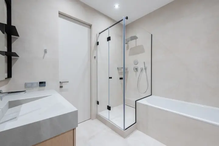Interior of modern light bathroom with bathtub and shower next to sink with cabinet near door