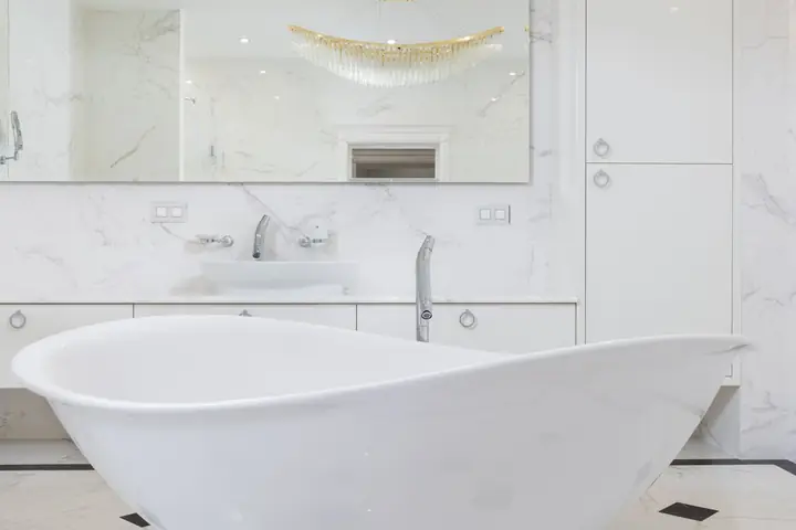 Interior of marble white modern bathroom with mirror reflecting shimmering huge chandelier in apartment