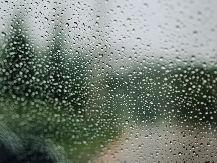 A close-up of raindrops on a window, blurring the outdoor scene for a moody atmosphere